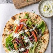 Sliced chicken shawarma served with pita bread, fresh vegetables, and creamy sauce.