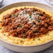A deliciously creamy bowl of Parmesan polenta, served with ground beef sauce garnished with fresh herbs.