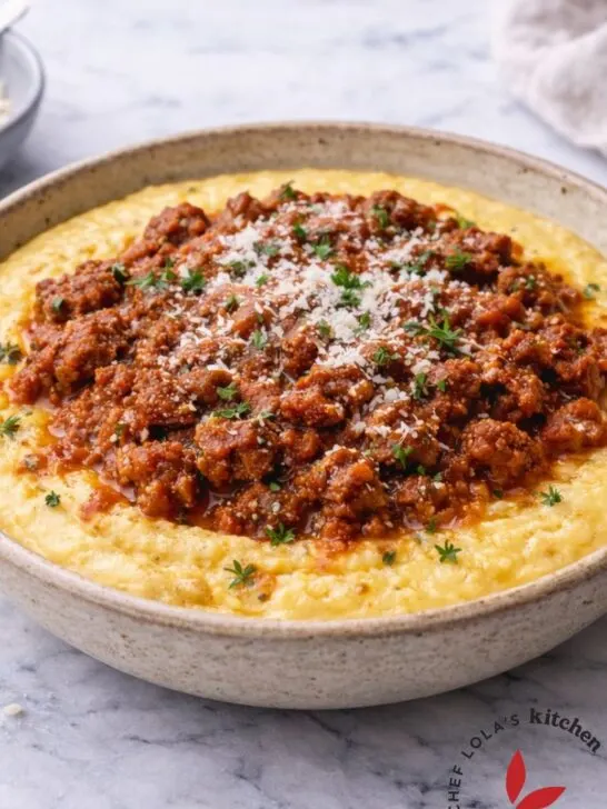 A deliciously creamy bowl of Parmesan polenta, served with ground beef sauce garnished with fresh herbs.