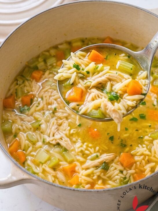 Lemon chicken orzo soup in a white Dutch oven with a ladle and a green checked towel