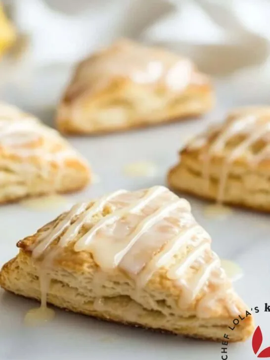 Freshly baked glazed lemon scones on a white plate, drizzled with glossy lemon glaze.