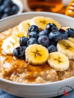 A hearty bowl of oatmeal porridge topped with banana slices, berries and honey