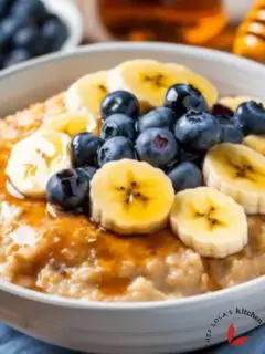 A hearty bowl of oatmeal porridge topped with banana slices, berries and honey