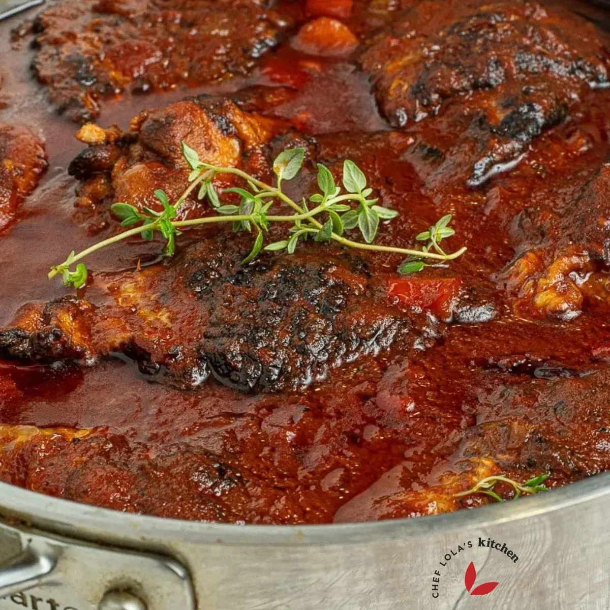 Jamaican brown stew chicken garnished with fresh thyme sprig.