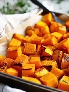 Tender oven-roasted butternut squash cubes on a parchment-lined baking sheet