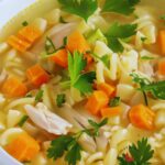 A bowl of chicken noodle soup garnished with parsley