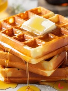 A stack of golden-brown classic waffles topped with melted butter and drizzled with maple syrup, ready to be served.