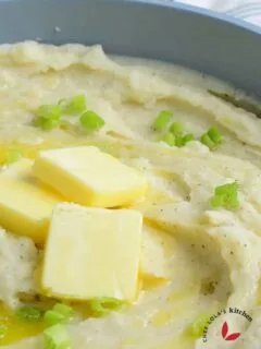 A bowl of creamy mashed potatoes topped with fresh green Onion and melted butter.