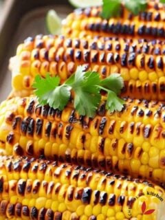 Grilled corn on the cob served on a tray and garnished with cilantro and lime