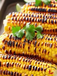 Grilled corn on the cob served on a tray and garnished with cilantro and lime