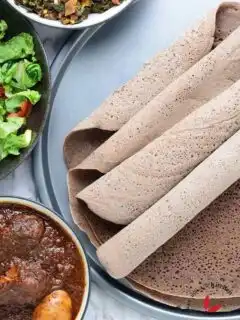 Injera in a tray with doro wat stew, salad, and Gomen wat served in bowls