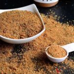 Jamaican Jerk spice blend in a white bowl beside a measuring spoon