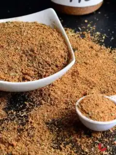 Jamaican Jerk spice blend in a white bowl beside a measuring spoon