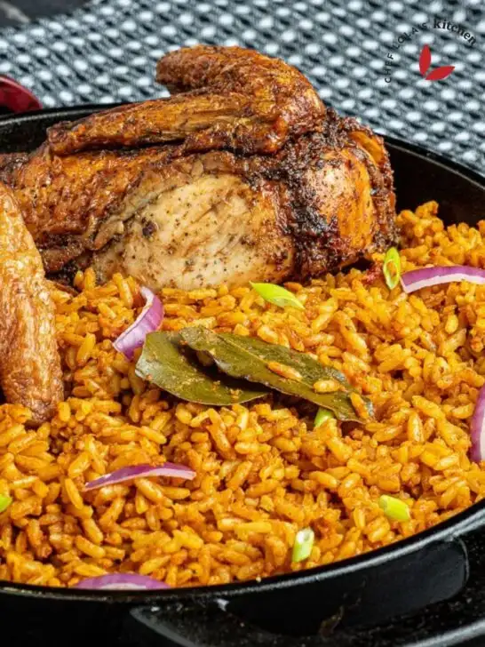 Jollof Rice with roasted chicken, garnished with bay leaves and red onion.