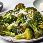 Golden-brown oven-roasted broccoli on a baking sheet, showcasing its deliciously crispy edges. Garnished with grated parmesan cheese.
