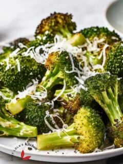 Golden-brown oven-roasted broccoli on a baking sheet, showcasing its deliciously crispy edges. Garnished with grated parmesan cheese.
