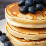 A close-up of a stack of pancakes on a plate with blueberries