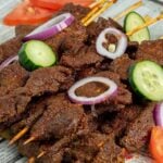 Nigerian Suya garnished with cucumbers, red onion, and tomtoes