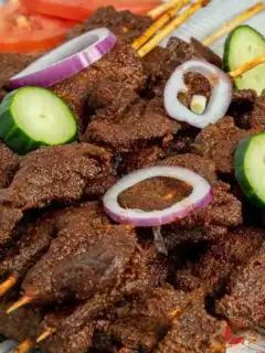 Nigerian Suya garnished with cucumbers, red onion, and tomtoes
