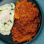 Sweet potato hash brown served with fried eggs and garnished with parsley.