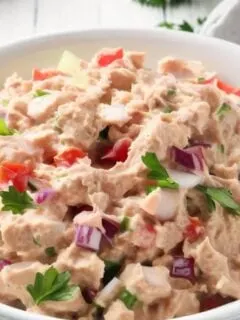 A bowl filled with creamy, freshly made tuna salad, garnished with finely chopped parsley.
