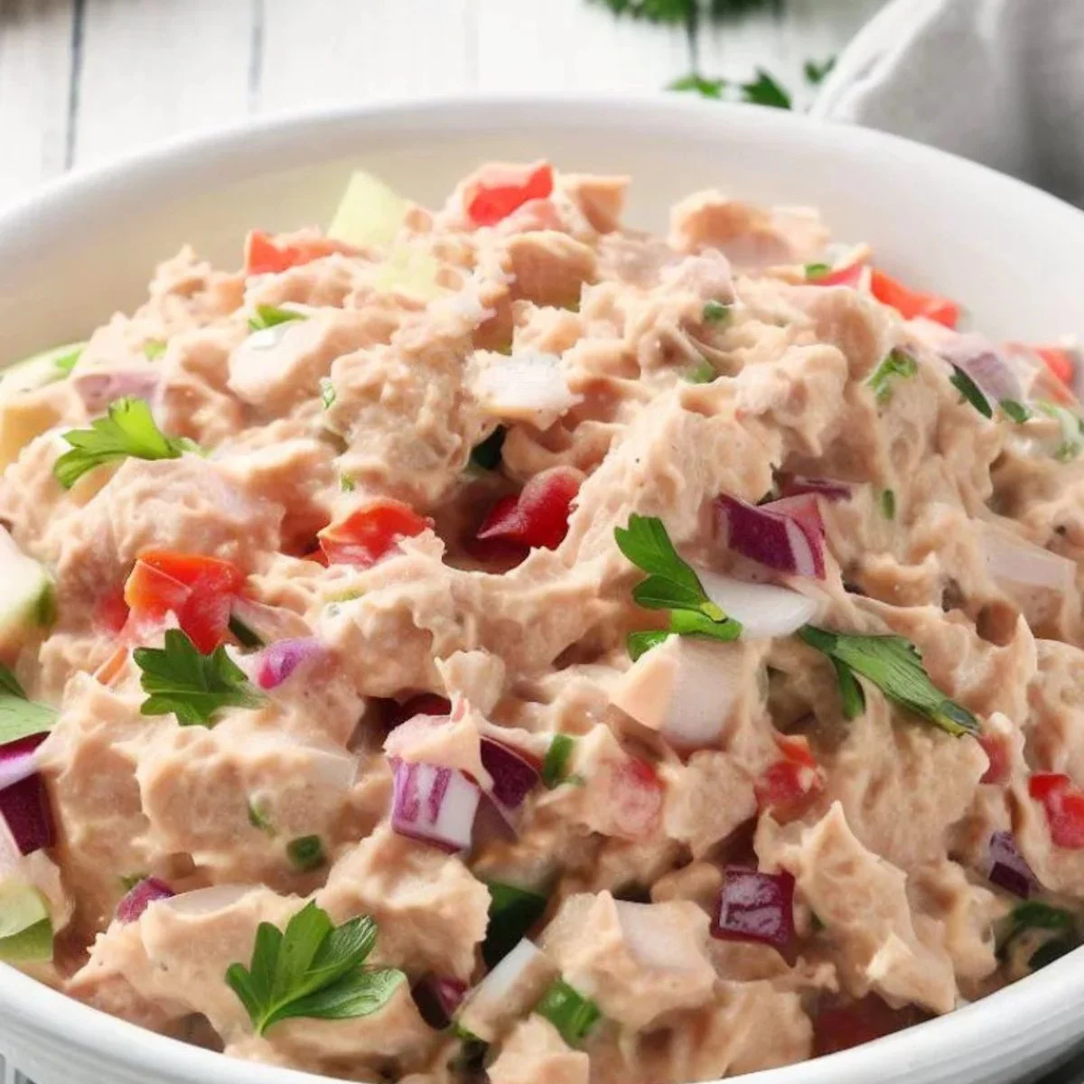 A bowl filled with creamy, freshly made tuna salad, garnished with finely chopped parsley.