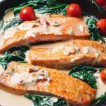 Creamy Tuscan Salmon in a cast iron skillet with tomatoes and spinach.