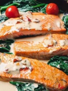 Creamy Tuscan Salmon in a cast iron skillet with tomatoes and spinach.