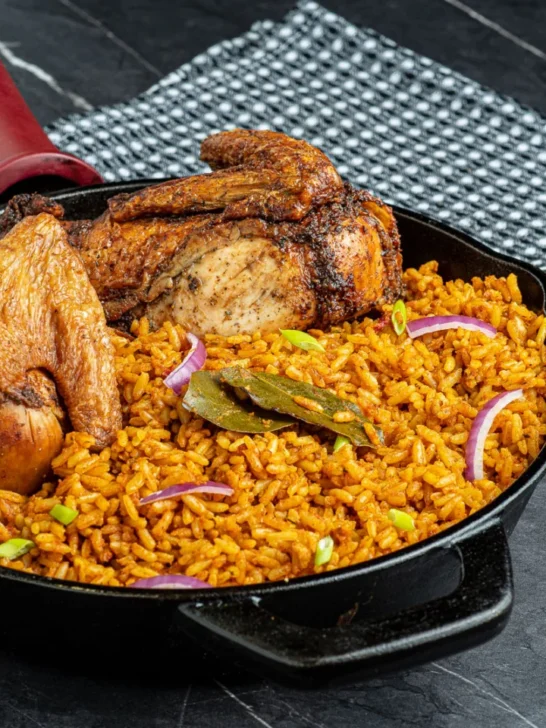 Jollof Rice with roasted chicken, garnished with bay leaves and red onion.
