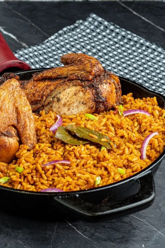 Jollof Rice with roasted chicken, garnished with bay leaves and red onion.