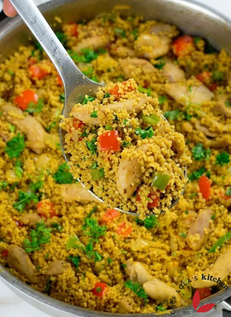 Close-up of seasoned couscous with tender chicken pieces and saut&eacute;ed vegetables in a light sauce.